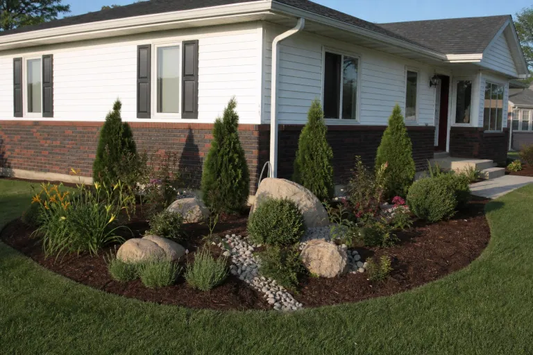New corner bed with arborvitae, boulders, and river rock